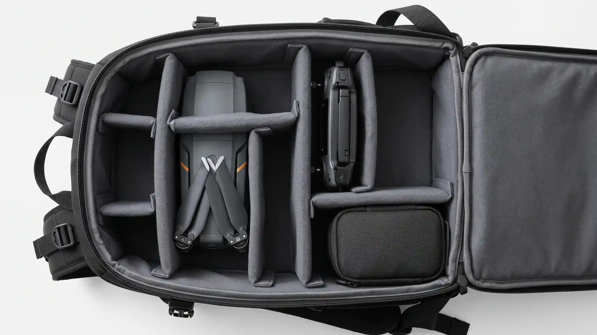 Overhead view of an open drone backpack interior with padded hook-and-loop dividers separating the drone body, controller, and LiPo battery pouch into firm closed compartments.