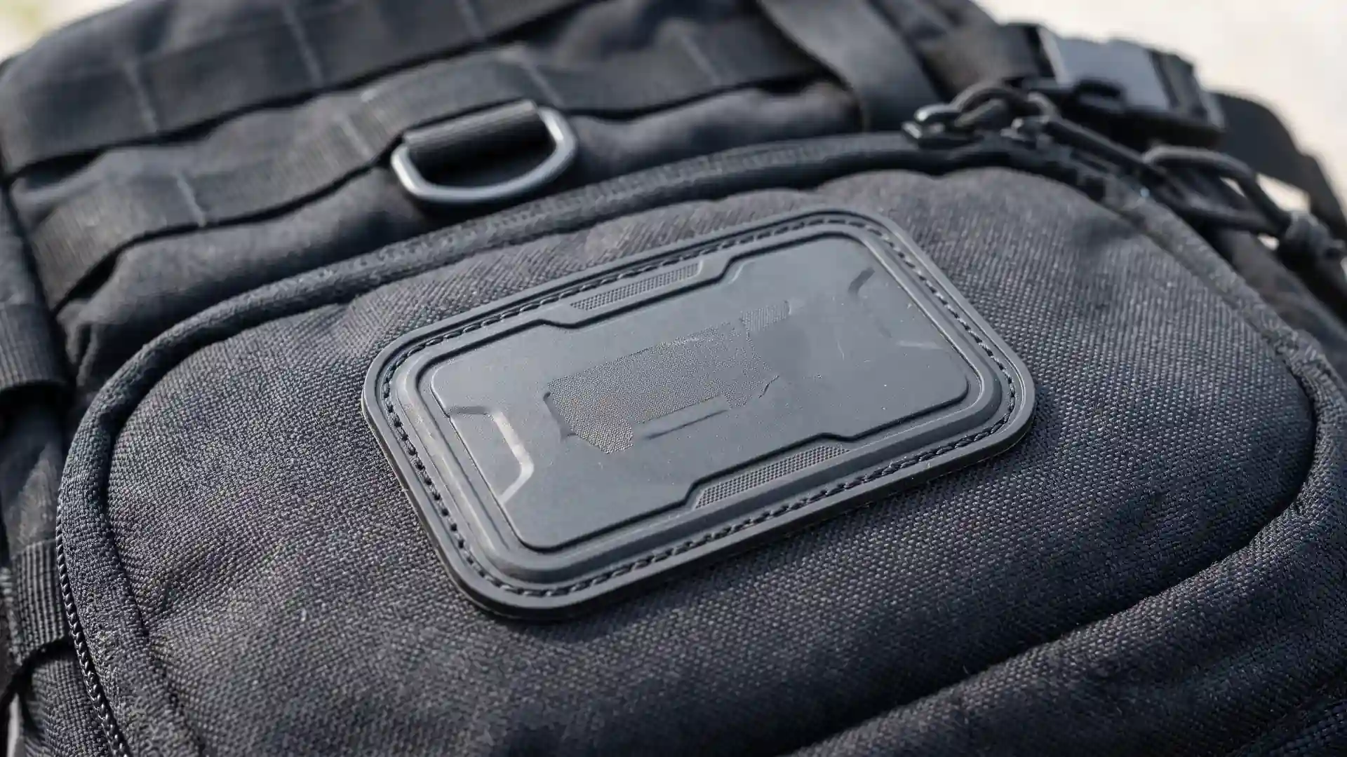 Raised molded TPU patch stitched along its shallow groove on a rugged tactical backpack panel for durable custom backpack logo methods.