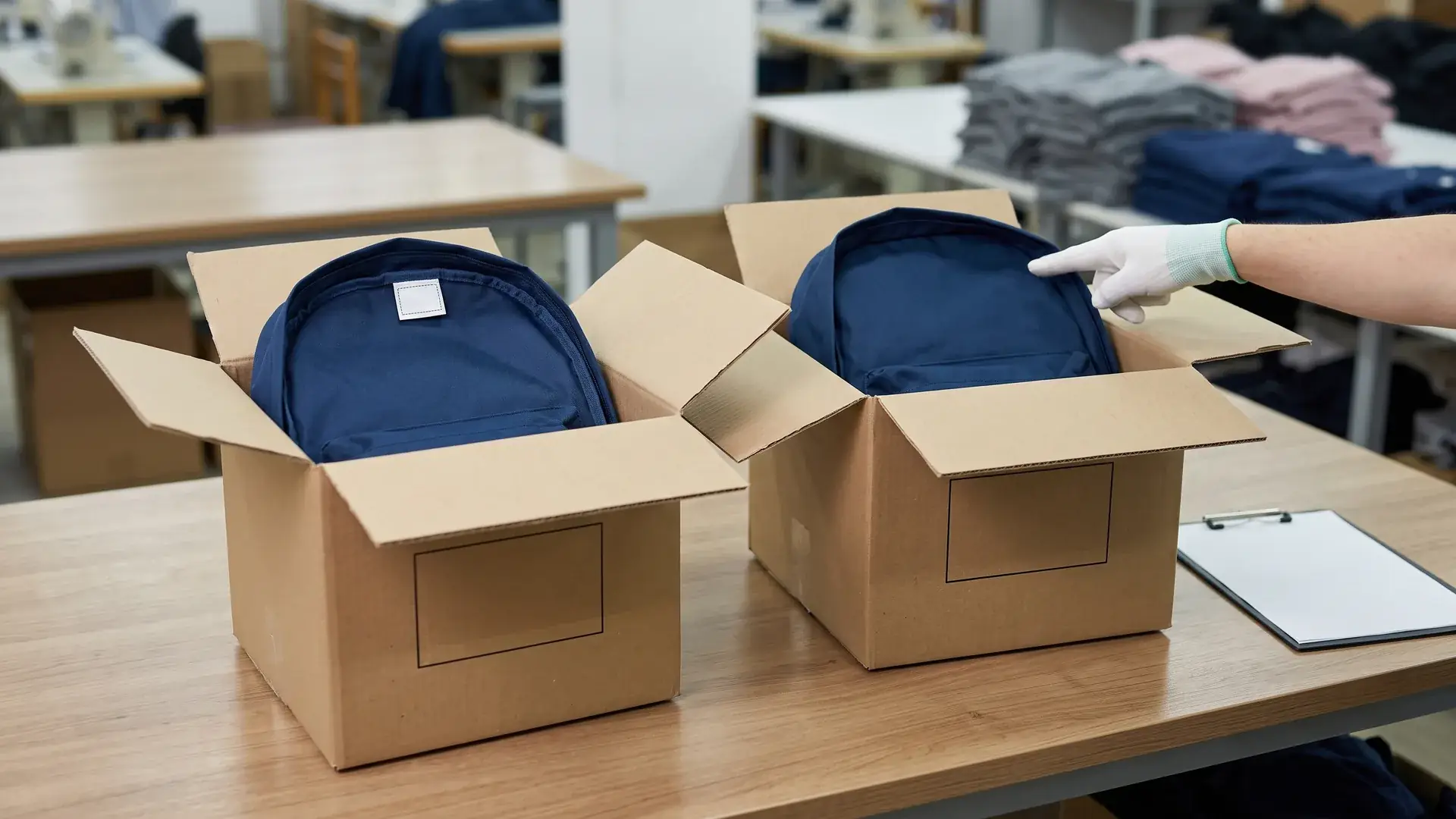 Pre-shipment inspection of two open export cartons where one backpack has a stitched country-of-origin label and the other is missing the label, showing a bag customs clearance hold risk.