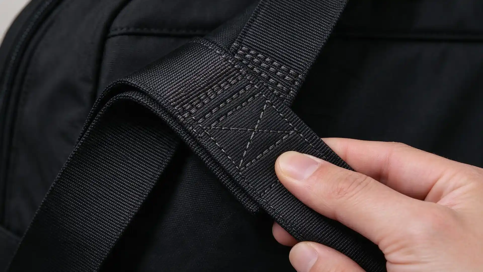 Macro close-up of a reinforced shoulder strap anchor on an electrician tool backpack showing dense bartack and box-x stitching in folded webbing.