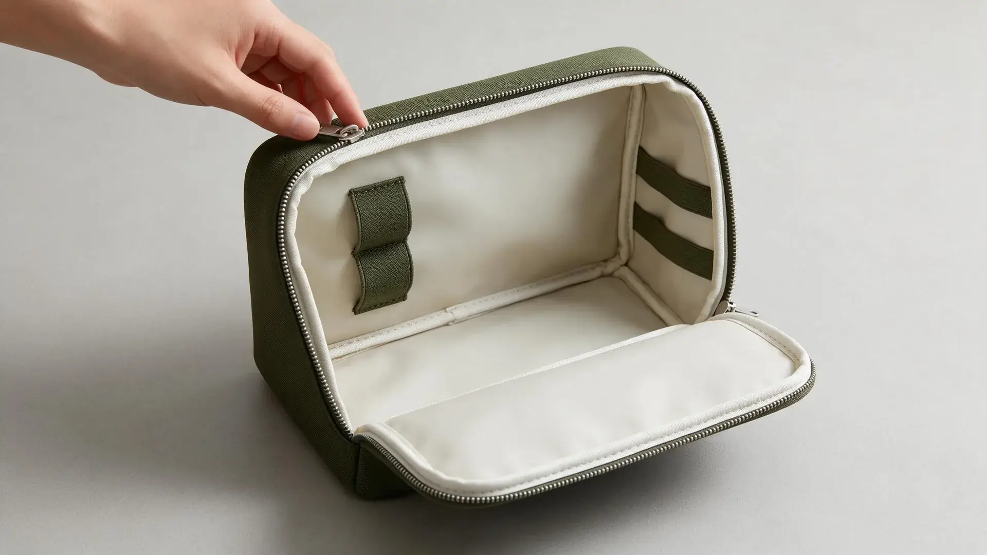 Open boxy makeup bag showing wipeable lining, bound seams, stiffened side panels, brush loops, elastic retainers, and a double-pull zipper, illustrating structure choices a makeup bag manufacturer uses to prevent collapse.